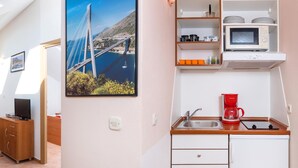 Een kleine keuken met een spoelbak, een rode koffiezetapparaat en een magnetron. Een lijst met een foto van een brug hangt aan de muur.