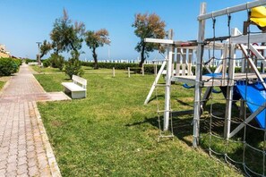 Un parque con un sendero pavimentado, un banco de madera y una estructura de juegos.
