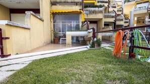 A courtyard with a grassy area, a yellow awning, and a window with a metal gate. - SE031 - Senigallia, two-room apartment facing the sea at the Piramidi residence (Cesano)