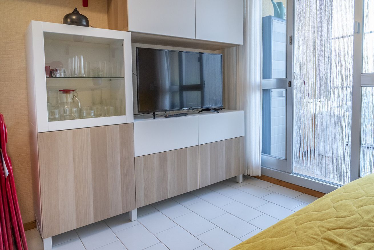 A modern room with a built-in TV, a glass cabinet with kitchenware, and a sliding glass door to the outside.