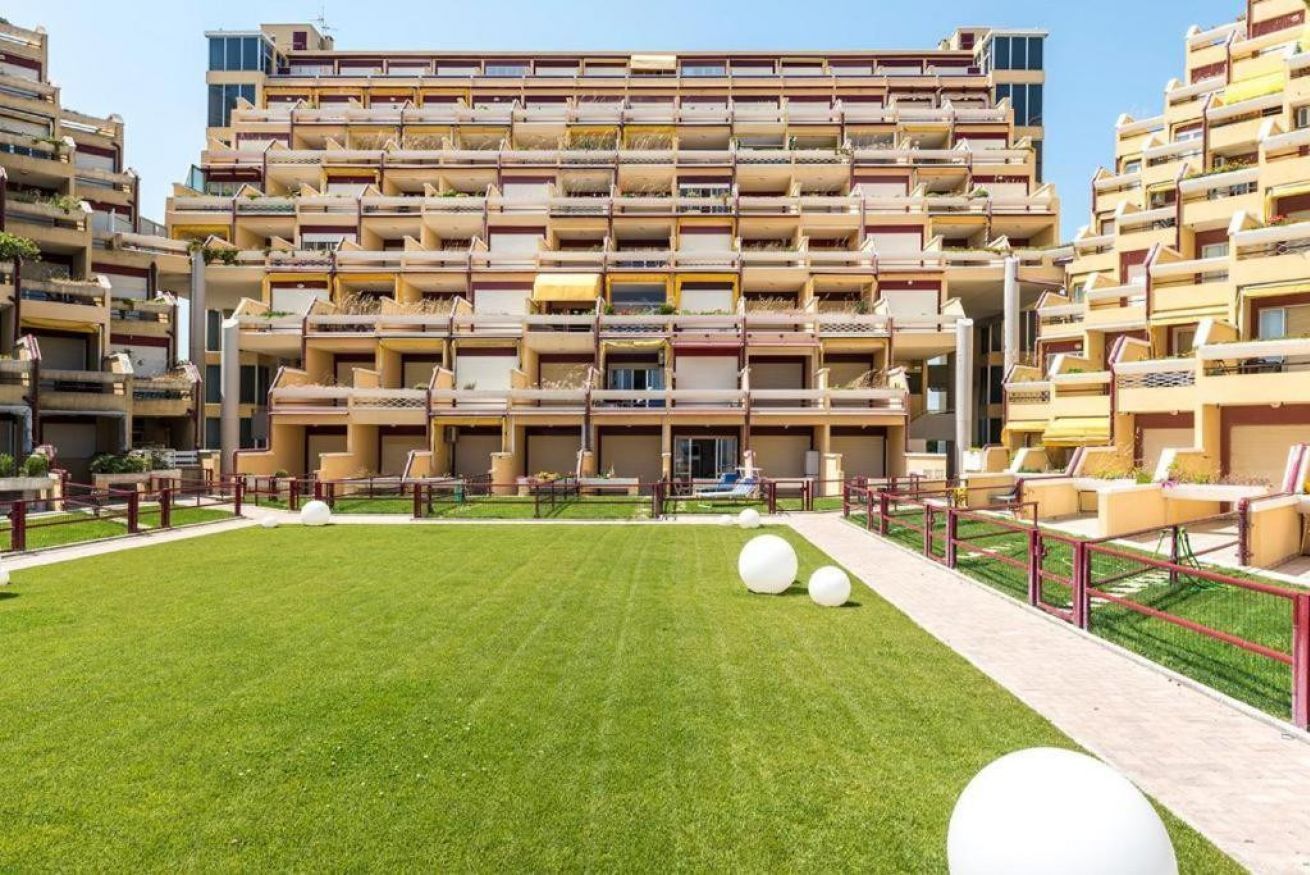 A multi-story residential building with balconies, a central courtyard with grass, and outdoor seating.