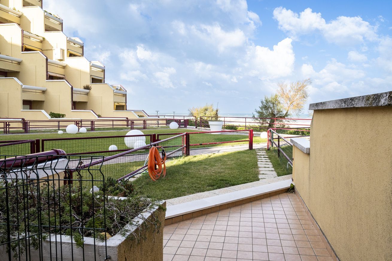 A residential building with balconies, a grassy area, and a clear sky.