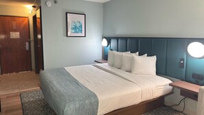 Un dormitorio con cama, lámparas de noche, una mesita de noche, un cuadro enmarcado en la pared y una puerta.