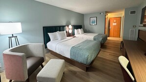 A hotel room with two beds, a desk, a chair, a lamp, and a picture on the wall.