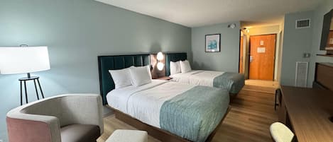 A hotel room with two beds, a desk, a chair, a lamp, and a picture on the wall.