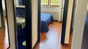 Une chambre avec un lit, une fenêtre, un radiateur et une salle de bain comprenant un lavabo et des toilettes.
