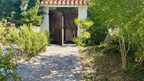 Un chemin de pierre mène à une entrée fermée par un portail, surmontée d’une structure dotée d’un toit en tuiles.