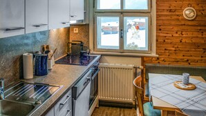 A compact kitchen with a window, a radiator, and a dining area with a table and chair. - Ferienhaus - Wald am Arlberg (Wald am Arlberg)