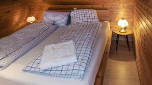 A wooden cabin bedroom with a bed, two pillows, a blanket, and two table lamps. - Ferienhaus - Wald am Arlberg (Wald am Arlberg)