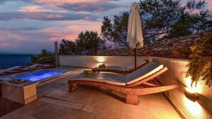 Terraço no telhado com hidromassagem, espreguiçadeiras e um painel de parede de pedra.