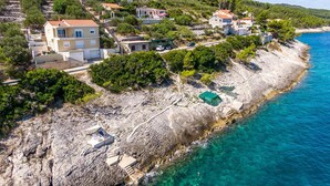 Zona residencial costeira com casas, linha costeira rochosa e mar azul cristalino.