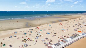 Een breed strand met tal van ligbedden en parasols, een heldere lucht en een rustige zee.
