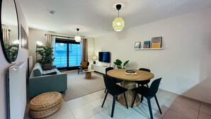 Een moderne woonkamer met een bank, een eettafel met stoelen, een televisie en een groot raam met uitzicht.