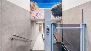 Een moderne lift met een bedieningspaneel, een handrail en een glazen deur.