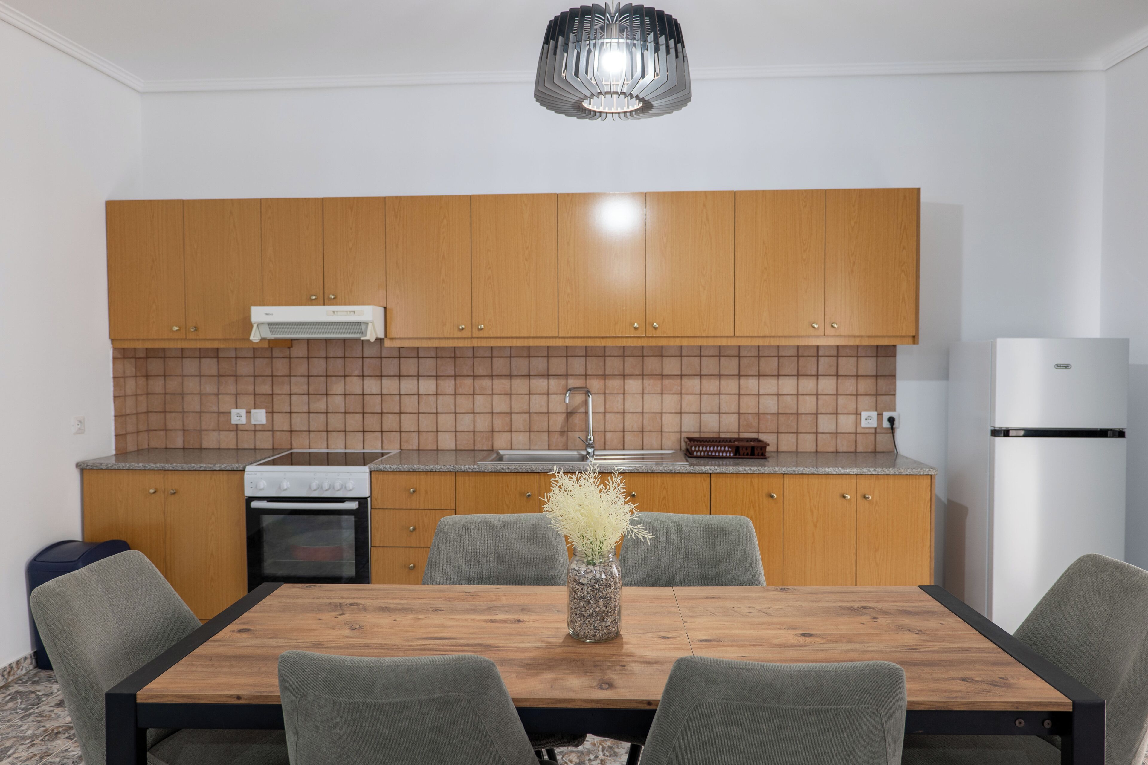 A modern kitchen with wooden cabinets, a built-in oven, a sink, and a dining area with a wooden table and four chairs.