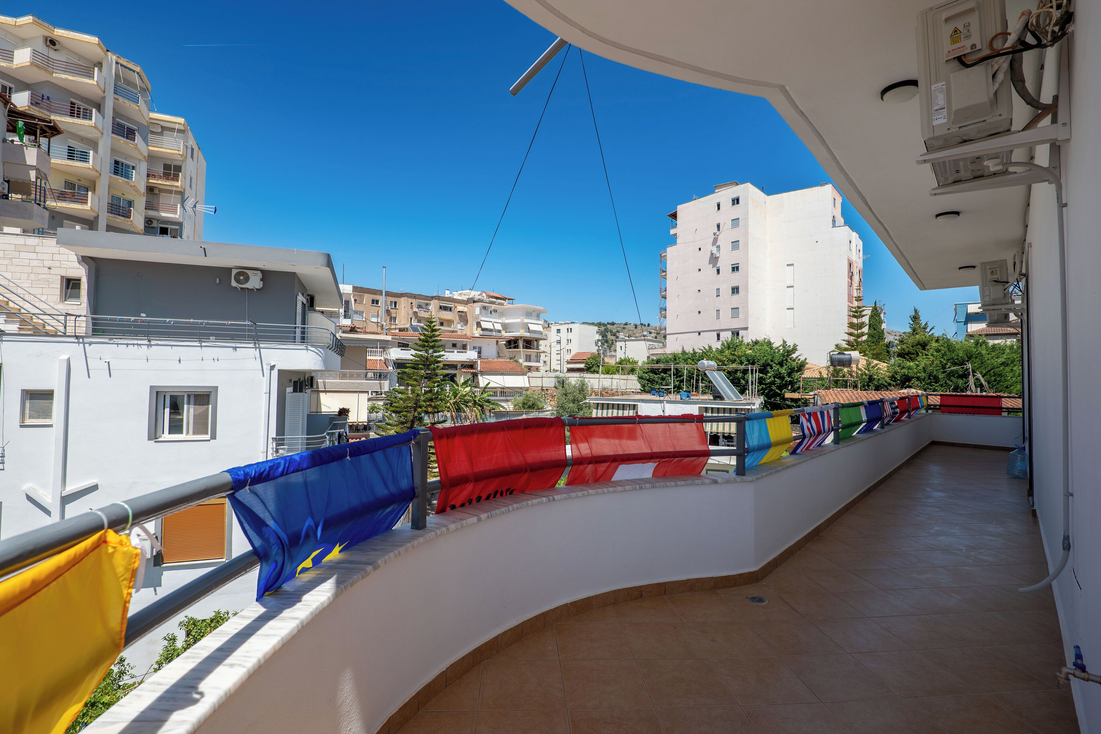 Un balcon donnant sur un quartier résidentiel, avec plusieurs immeubles et un ciel bleu dégagé.