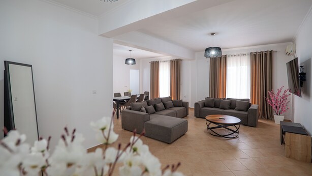 A modern living room with a sectional sofa, a coffee table, and a dining area with chairs. - Hoteleks (Sarandë)