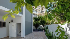 A narrow, paved corridor with a white door, a staircase, and a white wall with a blue railing. - Hoteleks (Sarandë)