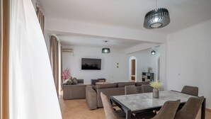 A modern living room with a sectional sofa, a dining table with chairs, and a TV mounted on the wall. - Hoteleks (Sarandë)