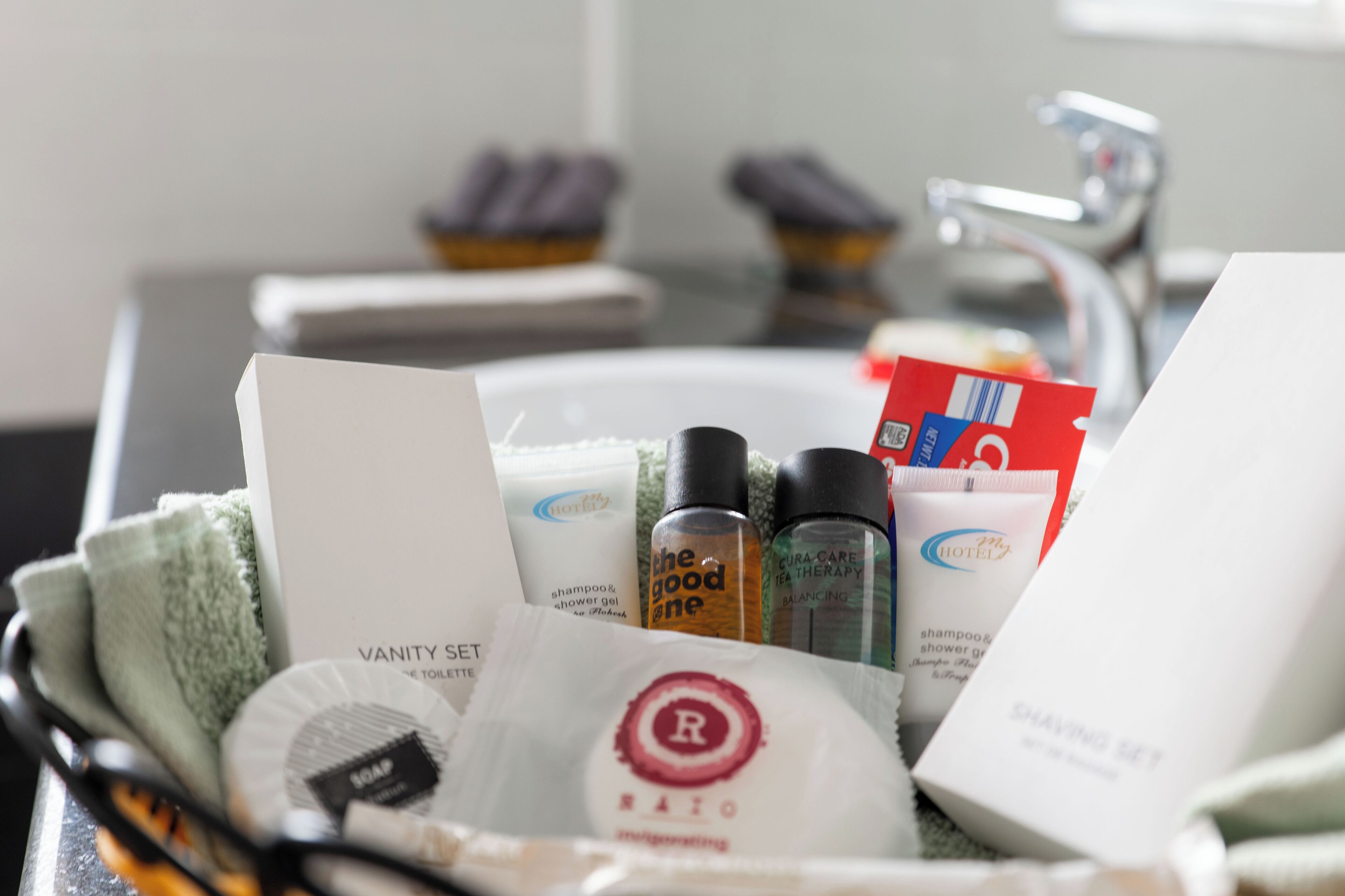 Ein Badezimmerwaschbecken mit verschiedenen Pflegeprodukten, darunter ein Schminktischset, Shampoo, Duschgel und ein Rasierer-Set.