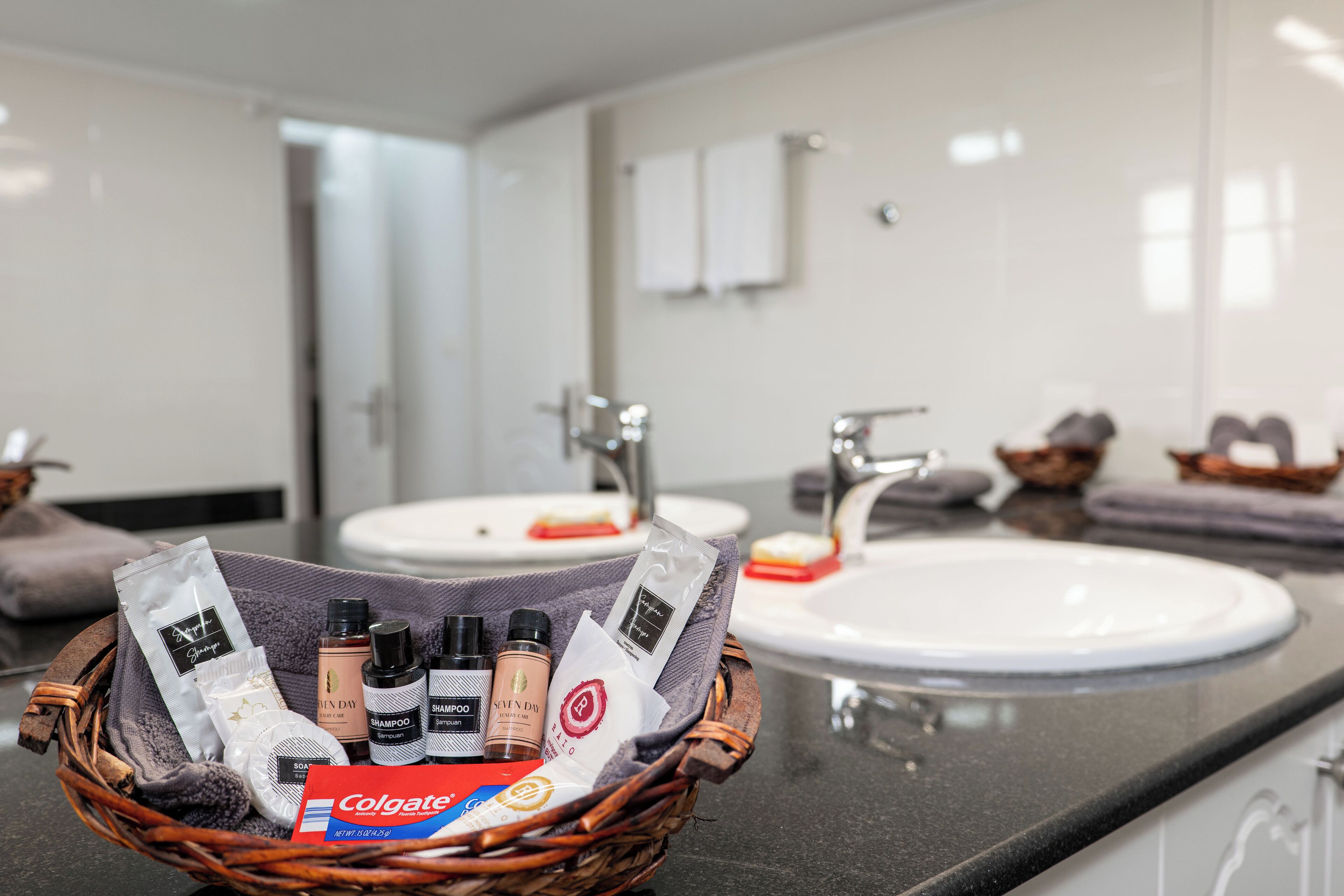 A bathroom with two sinks, a mirror, and toiletries in a basket.