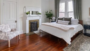 Een slaapkamer met een groot bed, een open haard, een deur en een raam met gordijnen.