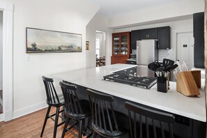 A modern kitchen with a large island, black bar stools, a microwave, and a refrigerator.