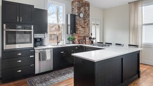 Een moderne keuken met donkere kastjes, een groot eiland en een wand met bakstenen.