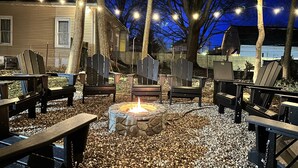 Een terras met Adirondack stoelen, een vuurkorf van natuursteen en sfeerverlichting.