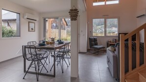 Un vaste espace dédié à la salle à manger, avec une longue table et des chaises, de grandes fenêtres et une vue sur l’extérieur.