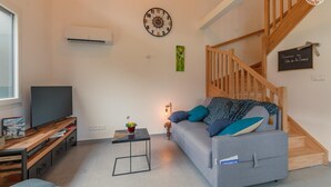 Un salon moderne avec un canapé gris, un escalier en bois et un téléviseur à écran plat.