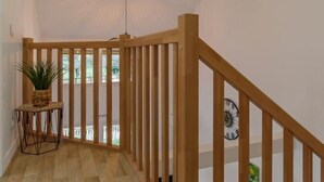 Un escalier en bois, doté d’une rampe, mène à un balcon. Une plante en pot est posée sur une petite table à côté de l’escalier.