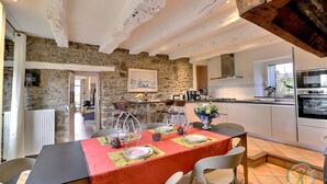 Un comedor con una mesa dispuesta para cuatro, paredes de piedra y una cocina al fondo.