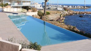 Un resort con piscina, una palmera y vista al puerto deportivo y al océano.