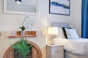 Ein Hotelzimmer mit einem Bett, einem Nachttisch, einer Lampe, einem an der Wand befestigten Regal mit Dekoration und einem Fenster mit Blick auf eine verschneite Landschaft.