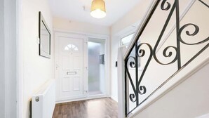 A hallway with a white door, a radiator, and a staircase with a black metal railing. - HP13 3BR Home w/Garden, WiFi &Easy Transport Links (High Wycombe)