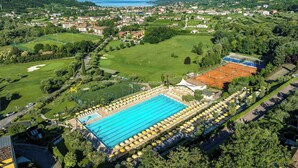 A large swimming pool with sun loungers and umbrellas, surrounded by lush greenery and a view of the sea.