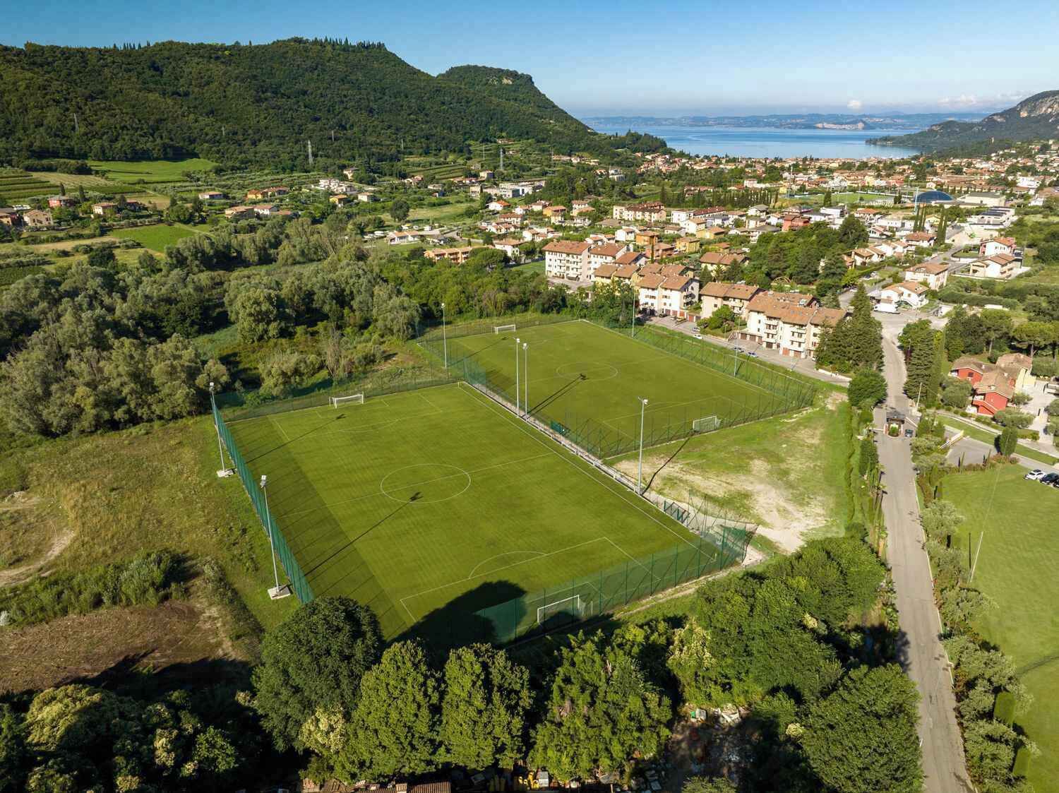 Vista aèria d'una vila amb un camp de futbol gran i verd, envoltat d'edificis residencials i arbres.