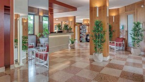 A hotel lobby with a checkered floor, wooden paneling, a reception desk, and several potted plants.