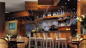 A bar area with multiple shelves of liquor bottles, wicker chairs, and a bar counter.