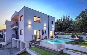 A modern two-story building with a swimming pool, outdoor seating, and a well-maintained lawn.