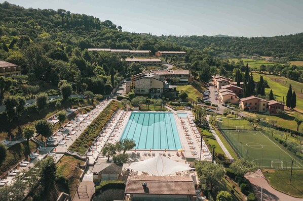 Un complexe hôtelier doté d’une grande piscine, d’un court de tennis et de plusieurs bâtiments abritant les chambres, le tout entouré d’une végétation luxuriante.