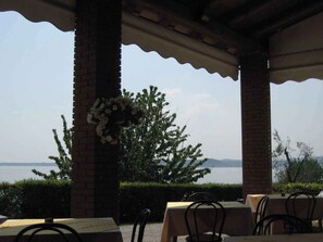 A covered outdoor seating area with brick pillars, tables with chairs, and a view of a body of water and distant hills.