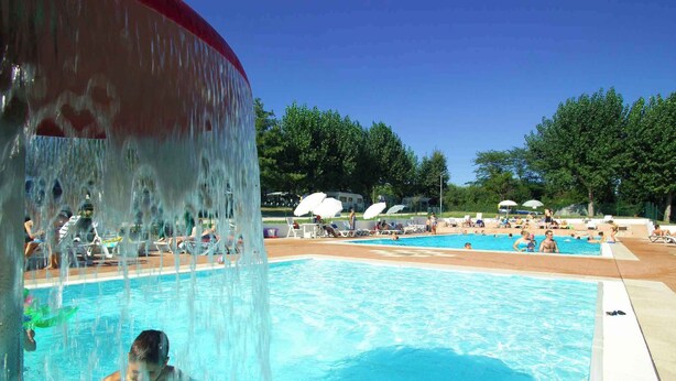 A swimming pool with a water feature, surrounded by lounge chairs and umbrellas.