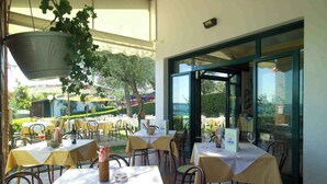 An outdoor dining area with tables set for guests, a hanging planter, and a view of the surrounding garden and buildings.