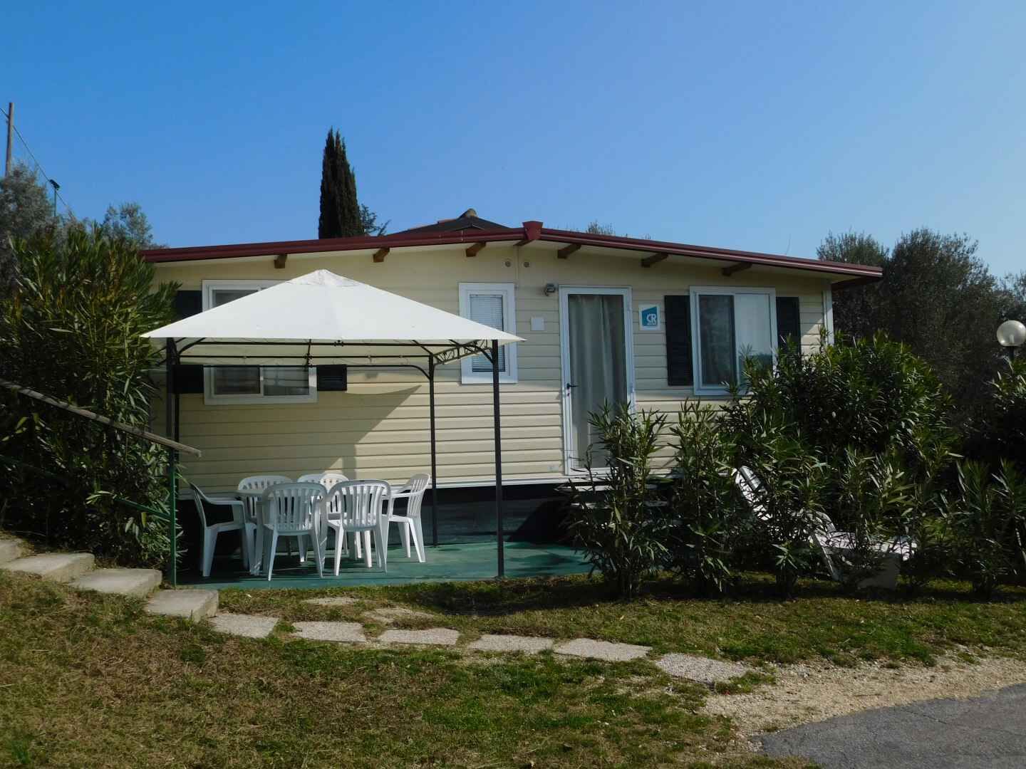 A single-story mobile home with a covered patio area, outdoor seating, and a small garden.