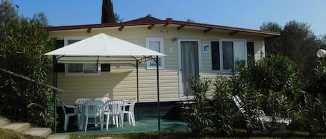 A single-story mobile home with a covered patio area, outdoor seating, and a small garden.