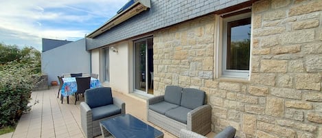 A patio with wicker furniture, a stone wall, and a tiled floor.