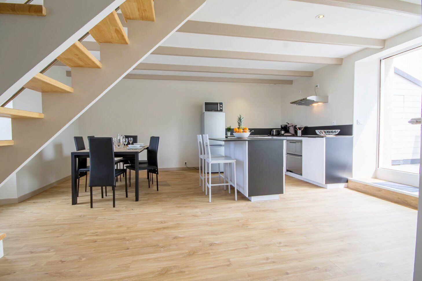 A modern kitchen with a dining area, wooden staircase, and large windows.