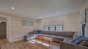 Una sala de estar moderna con un sofá seccional, una mesa de centro de madera y un ventanal con persianas.